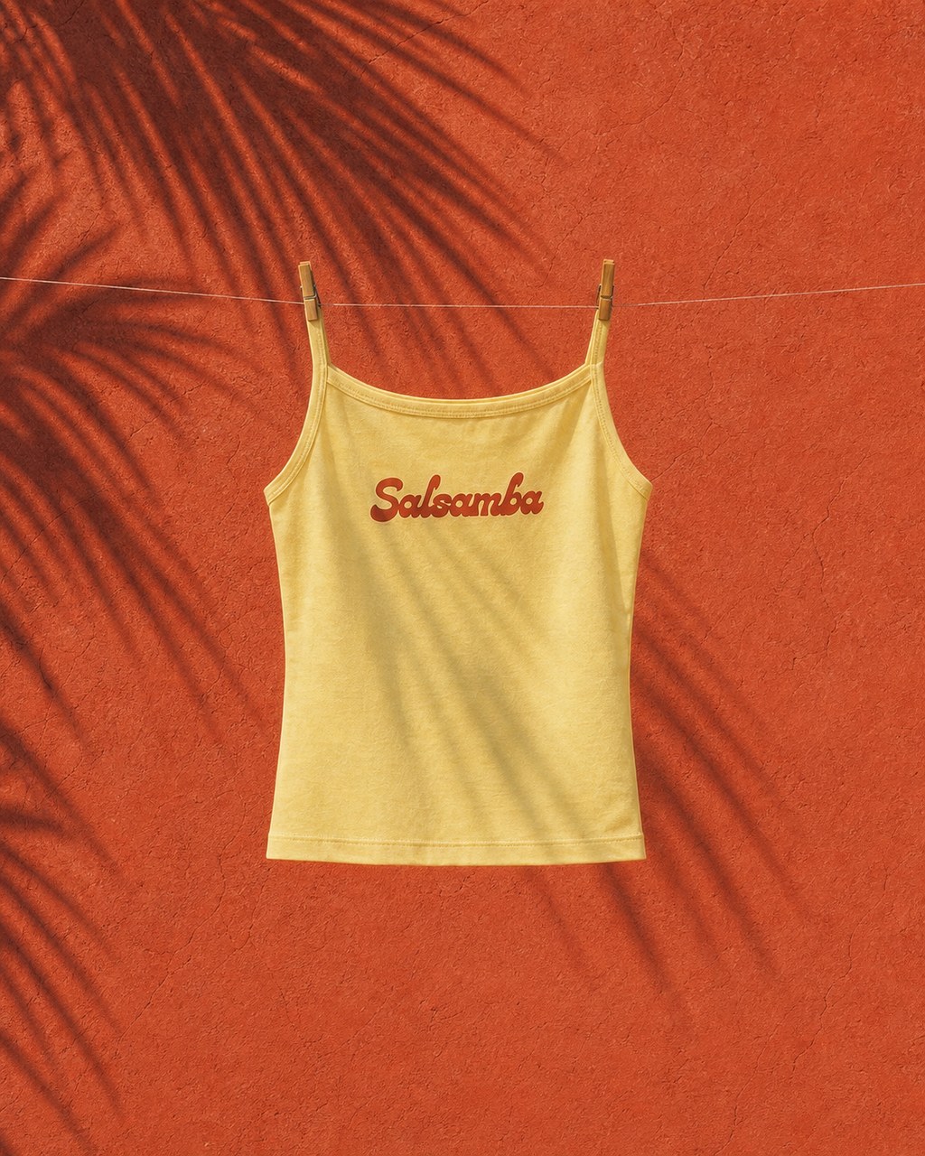 The baby-yellow Salsamba tank hanging from a clothesline against a terracotta wall